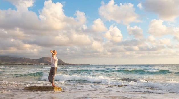 Relaxed woman enjoying sun, freedom and life an beautiful beach in sunset. Young lady feeling free, relaxed and happy. Concept of vacations, freedom, happiness, enjoyment and well being.