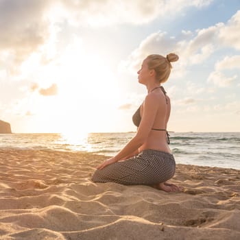 Active young woman streching and practicing yoga on beach at sunset.