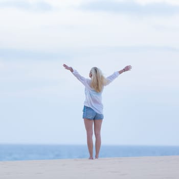 Relaxed woman enjoying freedom feeling happy at beach at dusk. Serene relaxing woman in pure happiness and elated enjoyment with arms raised outstretched up.