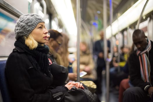 Beautiful blonde caucasian lady wearing winter coat traveling by metro in rush hour. Public transport.