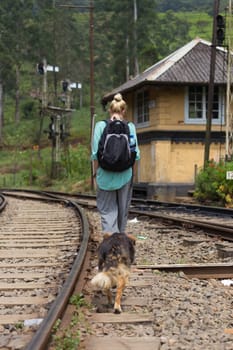 Female backpacker walking on railroad track followed by her best friend dog. Traveling adventure in Sri Lanka.