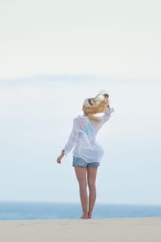Meditative, sensual blonde woman wearing white loose casual shirt on vacations, looking at horizon, enjoying peaceful early morning.