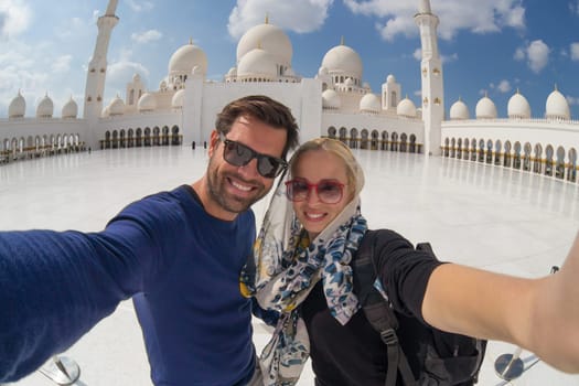 Tourist couple taking selfie in the courtyard of famous Sheikh Zayed Grand Mosque in Abu Dhabi, United Arab Emirates.