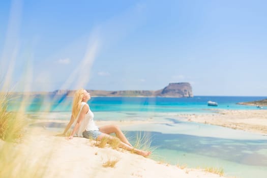 Relaxed woman enjoying sun, freedom and life an a beautiful sandy beach of Balos in Greece. Young lady feeling free, relaxed and happy. Vacations, freedom, happiness, enjoyment and well being.