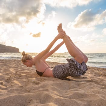 Active young woman streching and practicing yoga on beach at sunset.