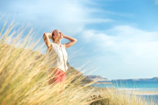 Relaxed woman, arms rised, enjoying sun, freedom and life an a beautiful beach. Young lady feeling free, relaxed and happy. Concept of vacations, freedom, happiness, enjoyment and well being.