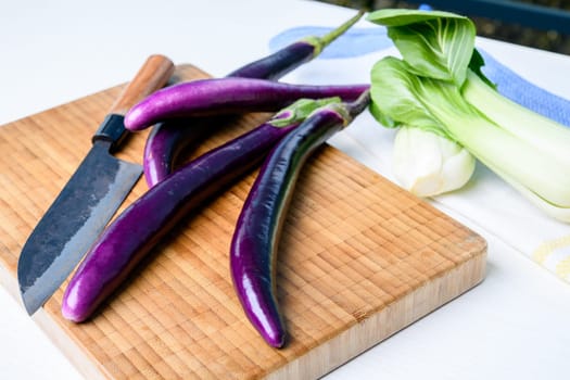 japanese eggplant on wooden board with cooking knife and pak choi salad