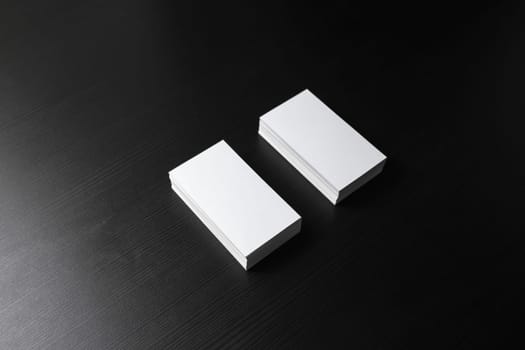Two blank business cards stacks at black wood table background.