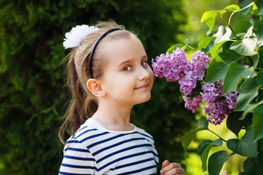 Little girl smelling lilacs in the garden. Beautiful spring day. Selective focus.