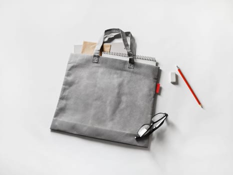 Blank gray shopping canvas bag, glasses, pencil and eraser on paper background.