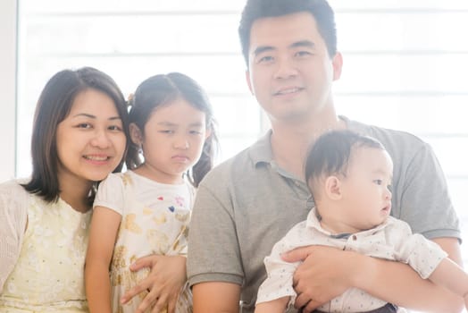 Happy parents and unhappy expression daughter. Asian family spending quality time at home, natural living lifestyle indoors.