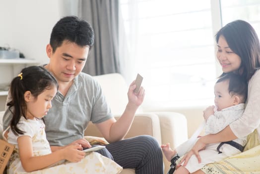 Online shopping with digital tablet pc and credit card. Happy Asian family at home, natural living lifestyle indoors.