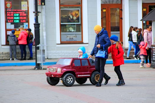 Girl driving the electric toy car on street. Mother watching her younger daughter driving toy car on street. Family vacation. Walking in city