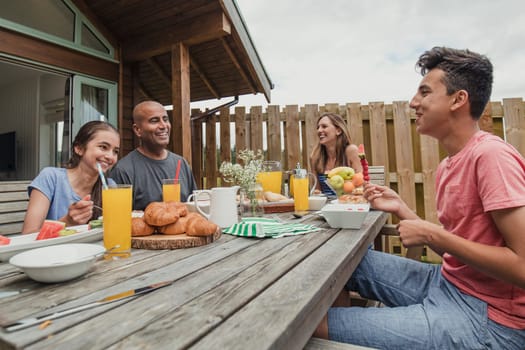 Family sitting outside holiday lodge and eating breakfast.