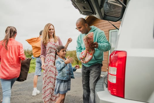 Little girl and mother helping her father unpack the car at holiday cottage.