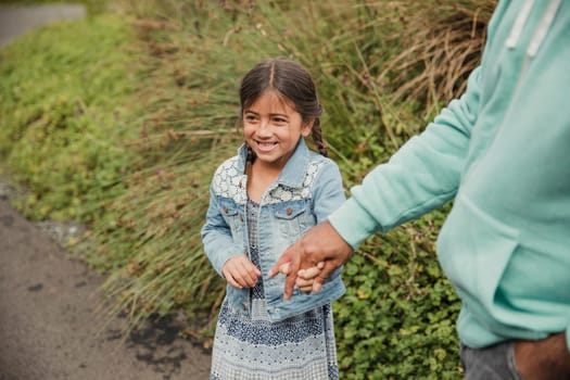 Little girl standing outside, laughing and holding her father's hand.