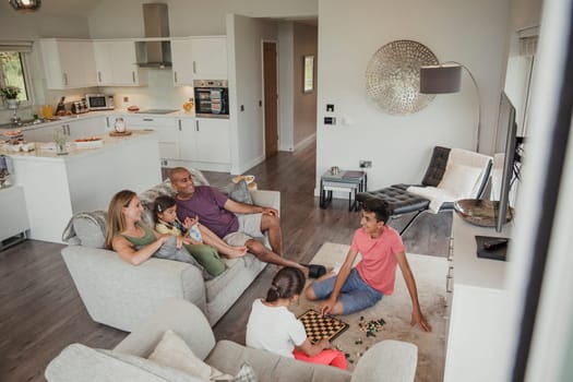 Family relaxing in their holiday home. Two of the children are playing chess while the rest of the family watch.
