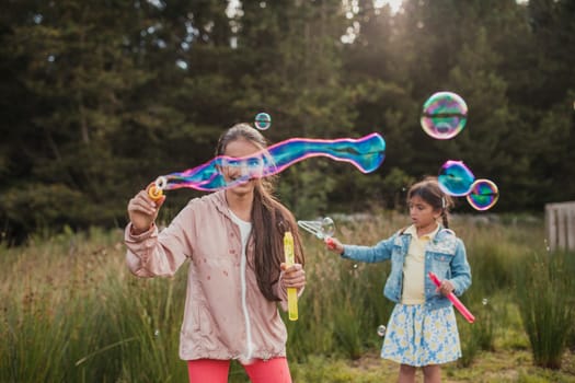 Two little girls creating bubbles in the woodlands on their holiday.
