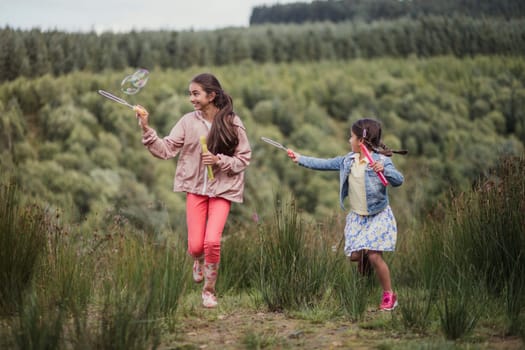 Young girls walking and playing with bubbles in woodland on holiday.