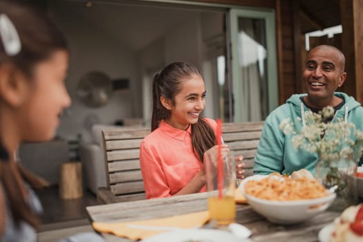 Little girl laughing with her family at the table outside holiday cottage.