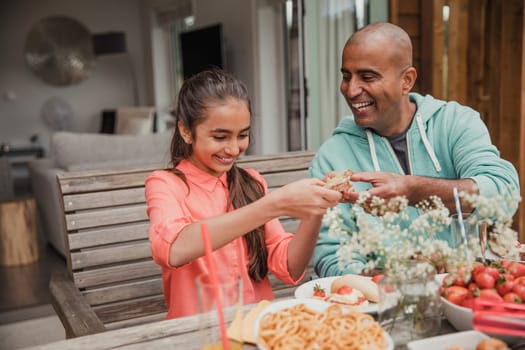 Father passing a sandwich to his daughter, sitting outside.