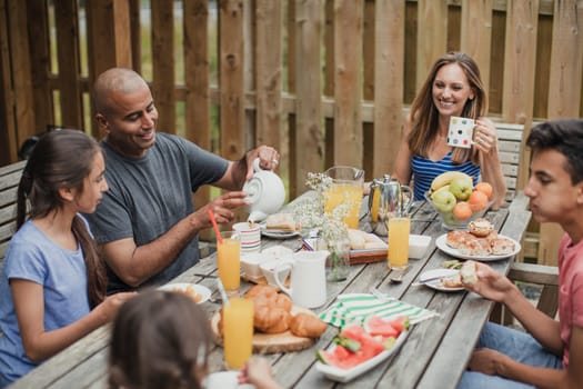 Family enjoying breakfast outside holiday cottage as father pours his first cup of tea.