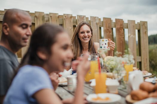 Focus on background of mother smiling at the breakfast table outside.