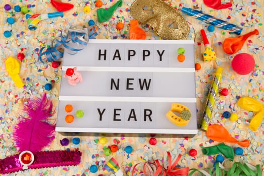 Light box with letters - HAPPY NEW YEAR - on colorful party decoration with streamers.