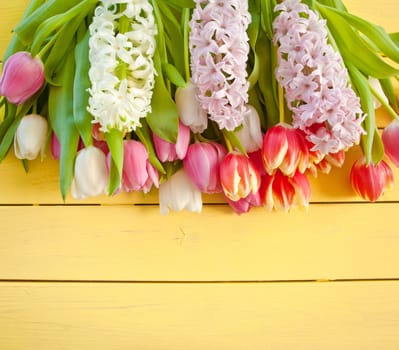 Fresh colorful tulips and hyacinths on yellow background made of wood