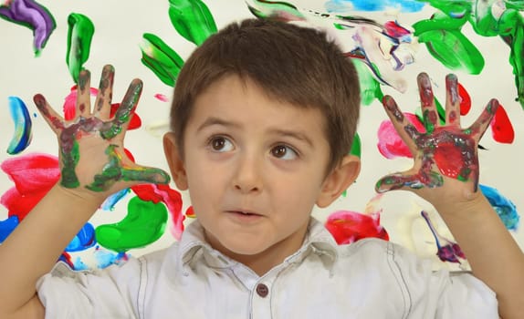 Little boy painting with hands with different color paint on his palms