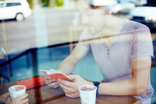 Young guy reading notes in notebook while sitting in cafe