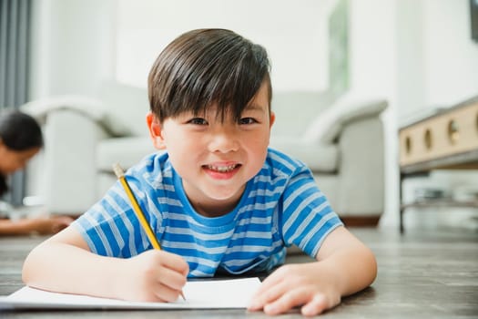 Little boy is smiling for the camera while lying on the floor as he is doing his homework.