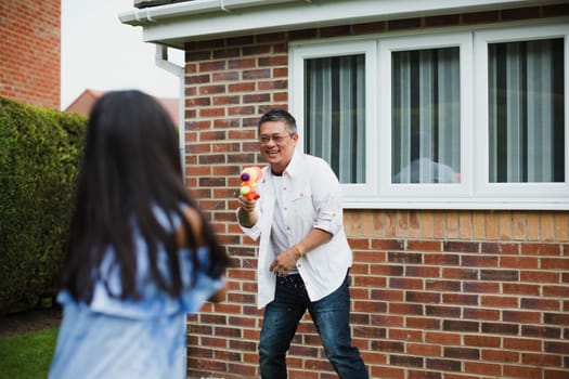 Little girl is having a water fight in the garden with her dad using water pistols.