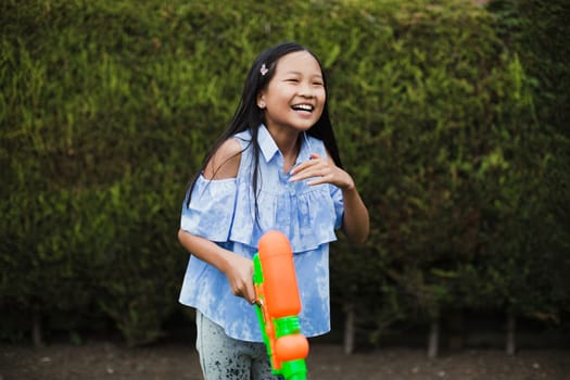 Little girl is having a water fight in the garden with her family. She is laughing with a water pistol in her hand.