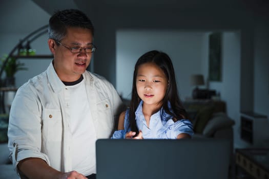 Little girl is getting help from her father while doing homework on the laptop at home.