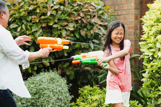 Little girl and her father are having a water fight in the garden with water pistols. The little girl is getting soaked and has her eyes closed as she tries to shoot back.