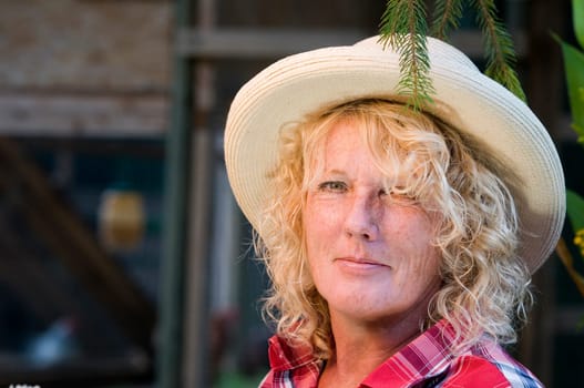 Side outdoor head portrait of a middle-aged woman with a straw hat smiling friendly into the camera.