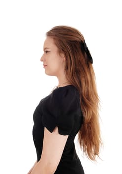 A lovely young woman standing in profile in a black dress with her.long brunette hair, isolated for white background.