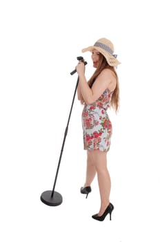 A beautiful young woman standing in front of a microphone in a dress.and singing, wearing a hat, isolated for white background.