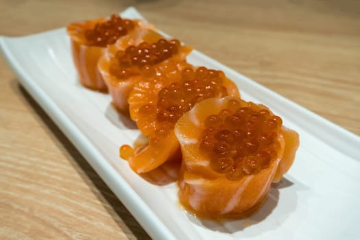 Fresh Raw Salmon Sushi roll with fish egg roe on long white plate closeup macro