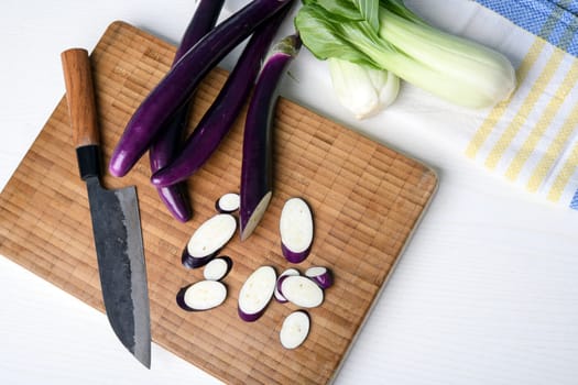 japanese eggplant on wooden board with cooking knife and pak choi salad