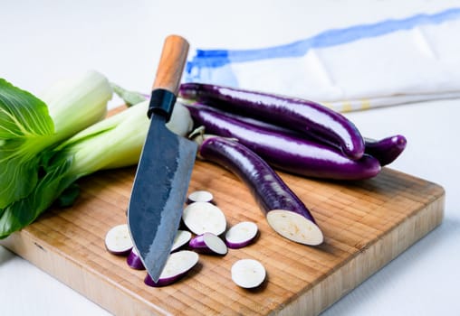 japanese eggplant on wooden board with cooking knife and pak choi salad