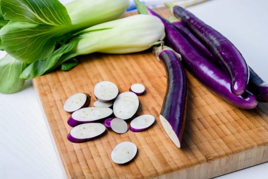 japanese eggplant on wooden board with cooking knife and pak choi salad