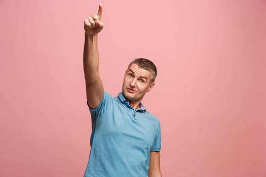 Wow. Attractive male half-length front portrait on pink studio backgroud. Young emotional surprised man pointing up. Human emotions, facial expression concept. Trendy colors