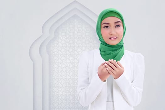 Smiling asian muslim woman raising hand and pray with white wall background