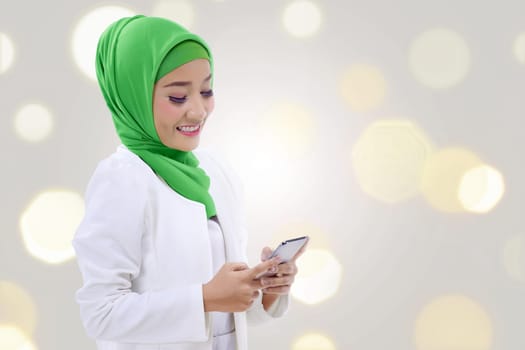 Happy asian muslim woman holding a phone over blur light background