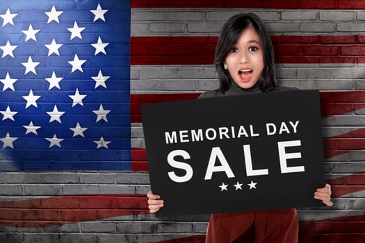 Young asian woman holding board with text memorial day sale with american flag background