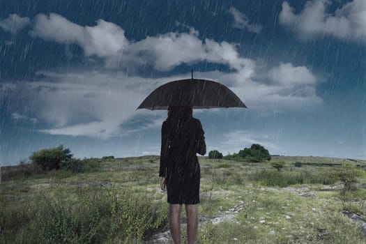 Businesswoman standing with an umbrella in rain over dark sky background