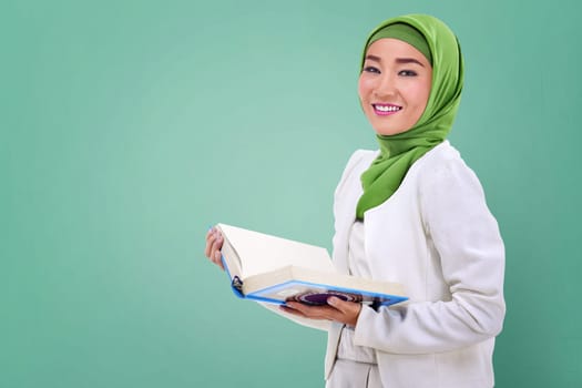 Young asian muslim woman holding the Koran over green background