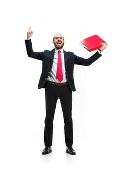 Full body or full-length portrait of businessman with red folder on white studio background. Happy bearded young man in glasses, suit, red tie standing in office. Business, career, success concept.